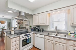 A modern kitchen with white cabinetry, a built-in oven, a dishwasher, and a stainless steel sink. - Breezy Bliss located near Coast Guard Beach Entrance, sleeps 9 (St. Simons Island)