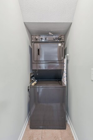 Un appareil combiné lave-linge et sèche-linge compact, en acier inoxydable, installé dans un espace étroit doté d’un plafond en pente.