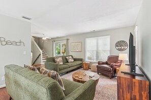 A living room with a green sofa, a brown leather chair, and a wooden coffee table. There is a staircase leading to another level. - Breezy Bliss located near Coast Guard Beach Entrance, sleeps 9 (St. Simons Island)