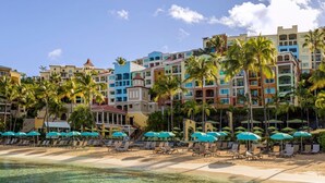 A beachfront hotel with multiple colorful buildings, a sandy beach with lounge chairs and umbrellas, and palm trees. - ST. THOMAS vacation resort in  the tropical U.S. Virgin Islands. (St Thomas)