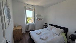 A bedroom with a bed, a radiator, a window, a wardrobe, and a bedside table. - A Cozy One-Bedroom Apartment in a Charming, Authentic Village (Saint-Fort-sur-Gironde)
