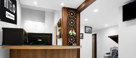 A reception desk with a wooden finish, a black computer, and a decorative panel with flags.