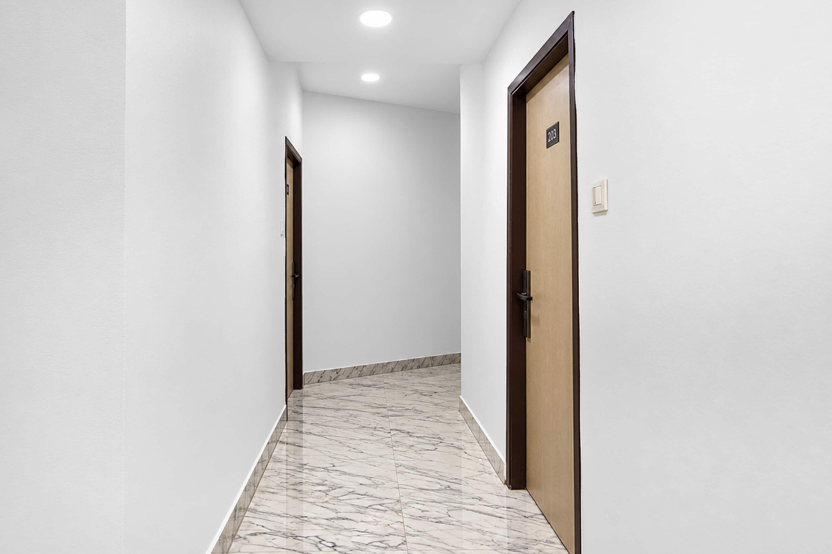 A hallway with white walls, a marble floor, and two doors, one with a number sign.