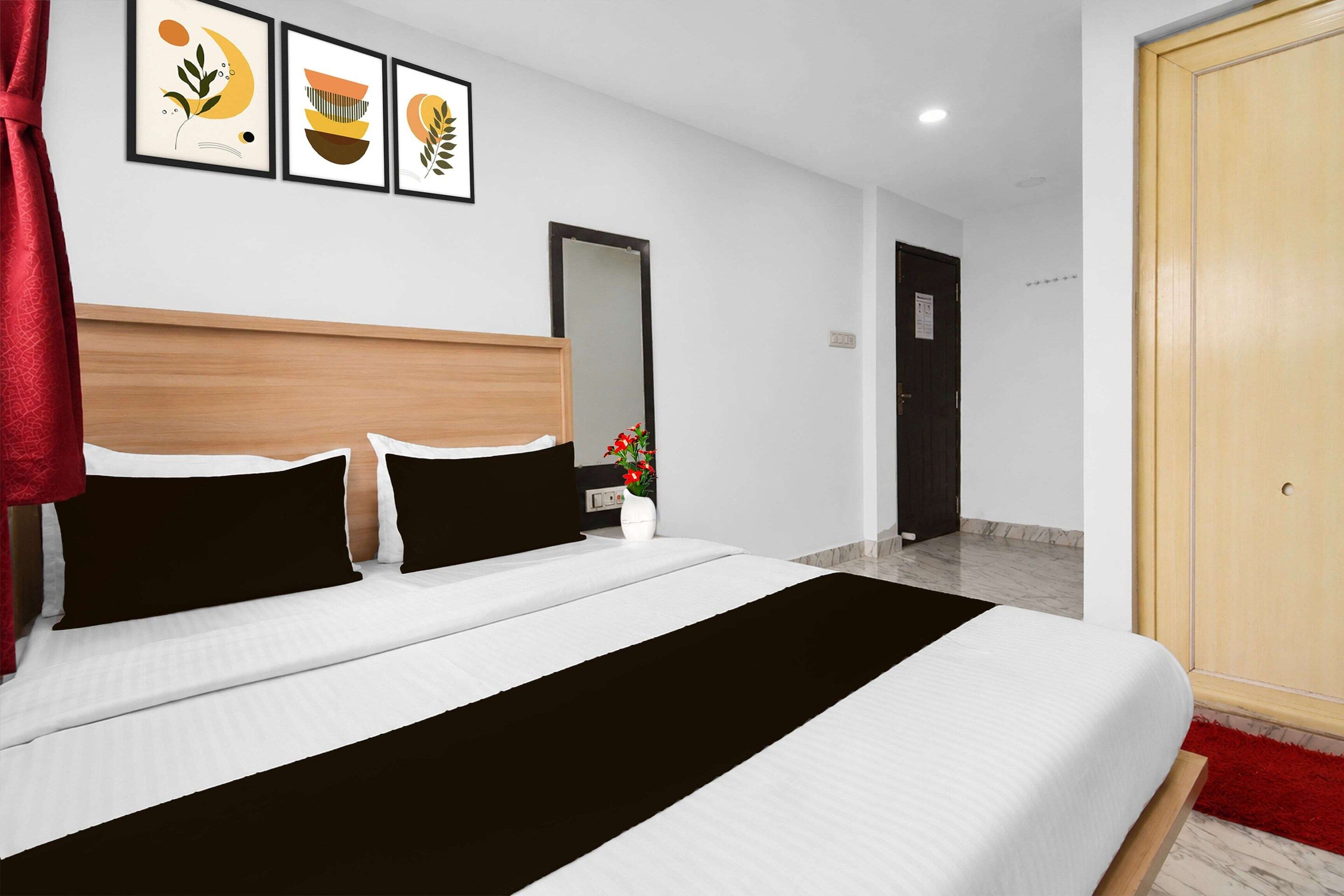 A hotel room with a bed, a mirror, a door, and three framed pictures on the wall.