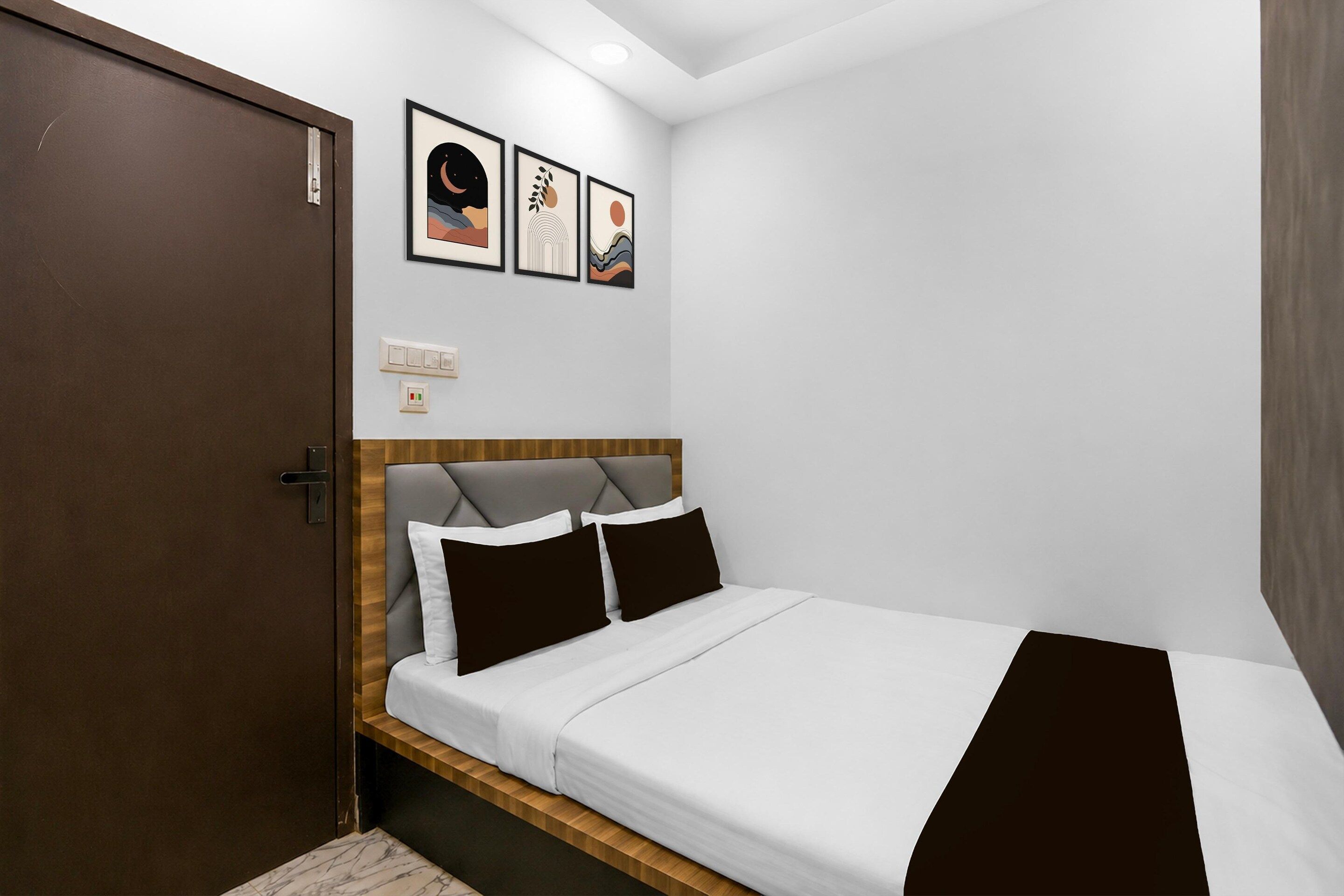 A hotel room with a bed, a door, and three framed artworks on the wall.