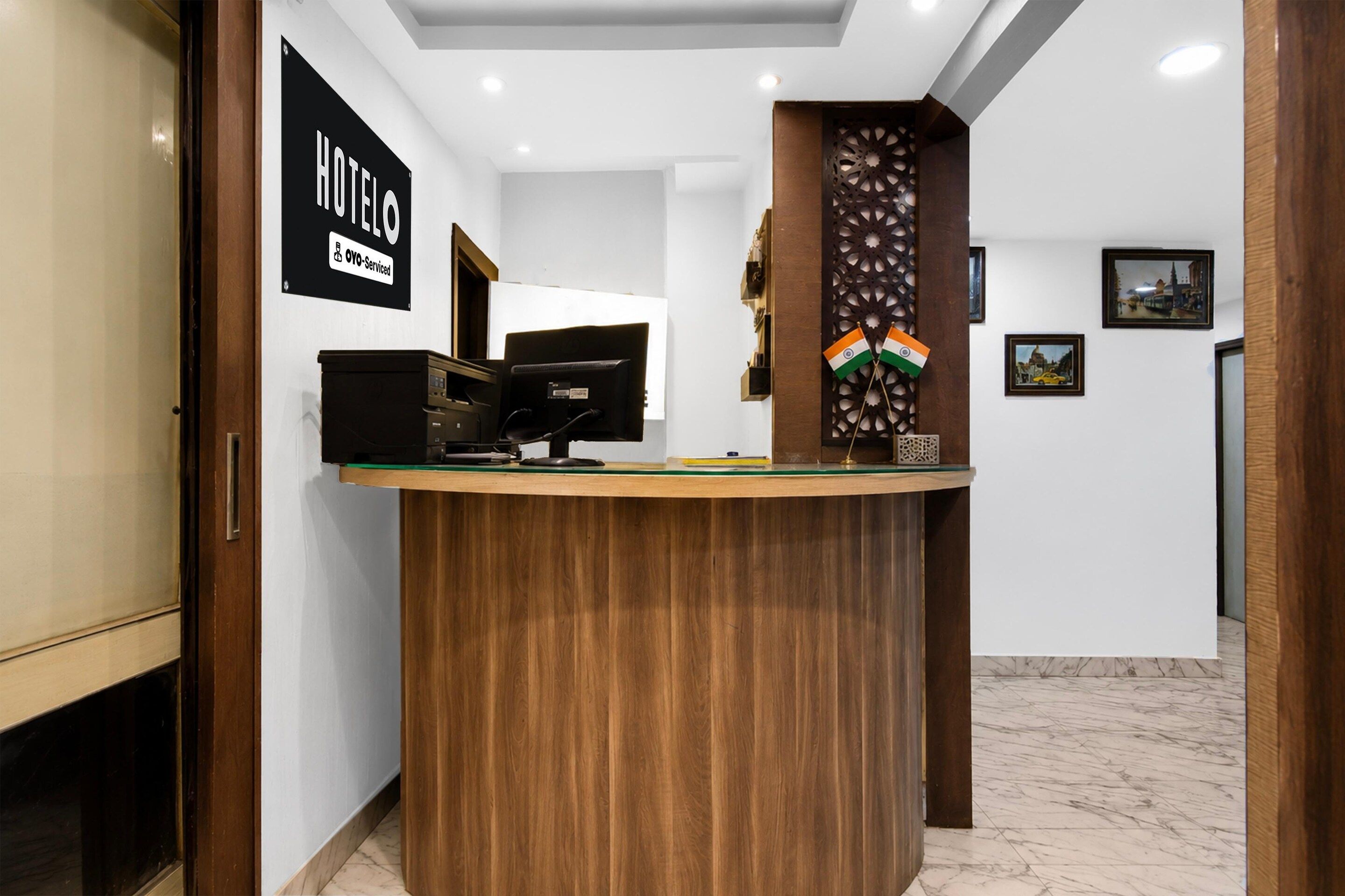 A hotel reception desk with a wooden finish, a black sign indicating it is serviced by OYO, and two Indian flags.