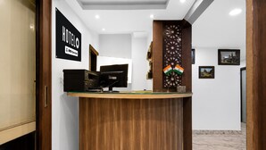 A hotel reception desk with a wooden finish, a black sign indicating it is serviced by OYO, and two Indian flags. - Hotel O Ripon Street SR Royale (Kolkata)