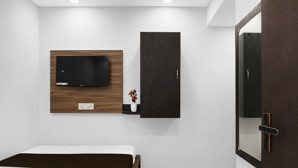 A bedroom with a bed, a wall-mounted TV, a dark cabinet, and a door with a mirror. - Hotel O Ripon Street SR Royale (Kolkata)