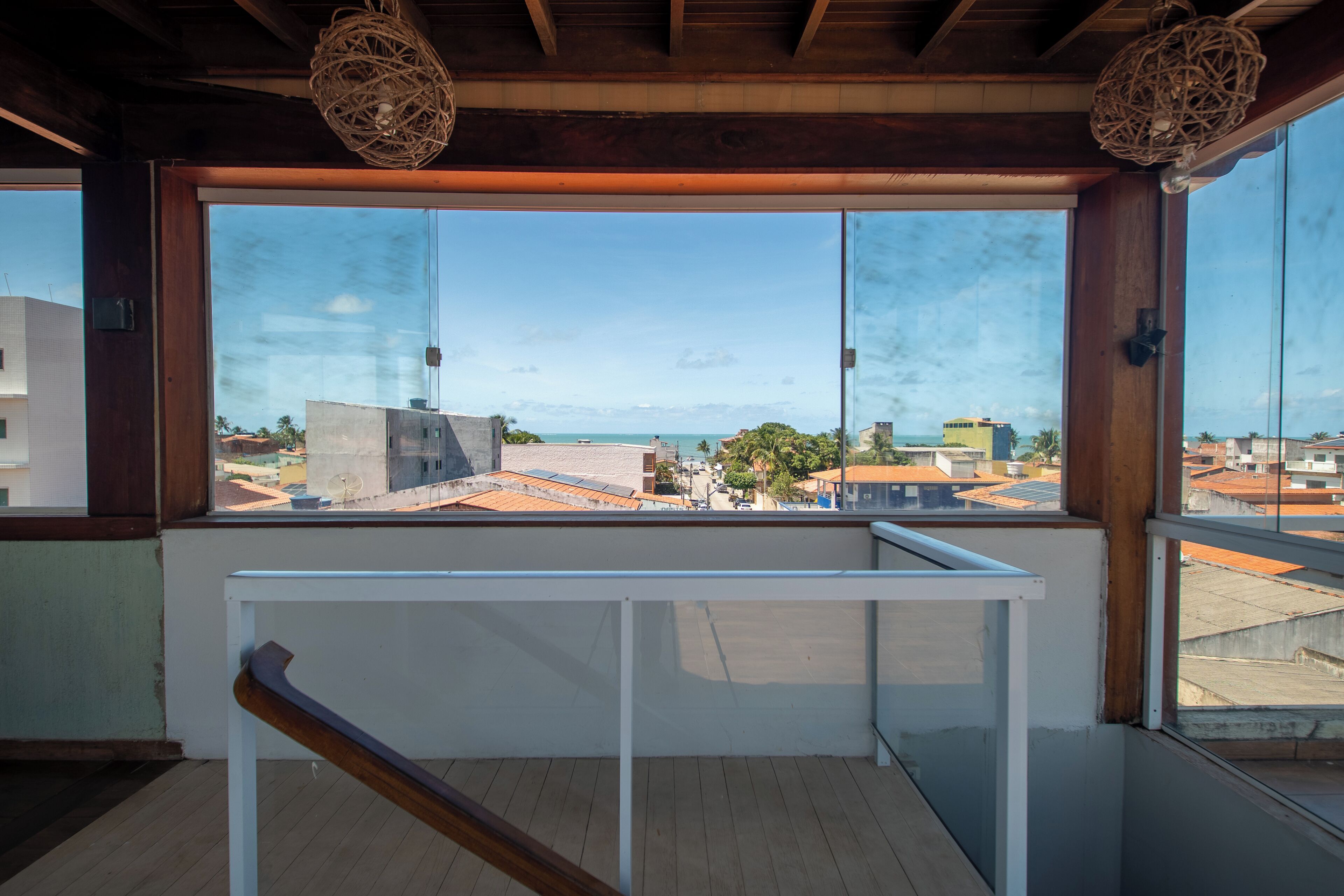 A balcony with a view of a coastal cityscape, wooden railings, and a clear sky.