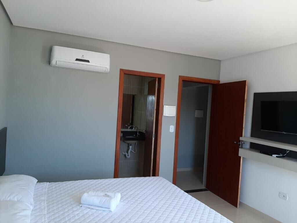 A hotel room with a bed, a television, an air conditioning unit, and a bathroom visible through an open door.