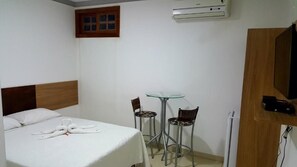 Una habitació d'hotel amb un llit, una taula petita amb cadires, un aparell d'aire condicionat i una porta de fusta.