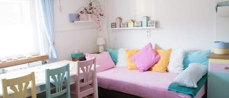 A cozy room with a bed, a table, chairs, and a shelf with decorative items.