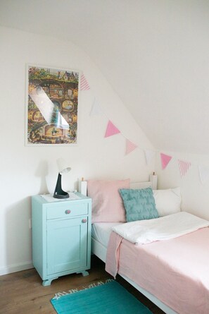 A bedroom with a bed, a nightstand, a lamp, a painting, and bunting on the wall.