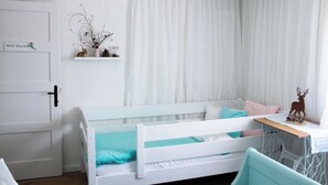 Habitació infantil amb bressol blanc, un taulell petit amb una decoració de cervís i una prestatgeria amb petits objectes.