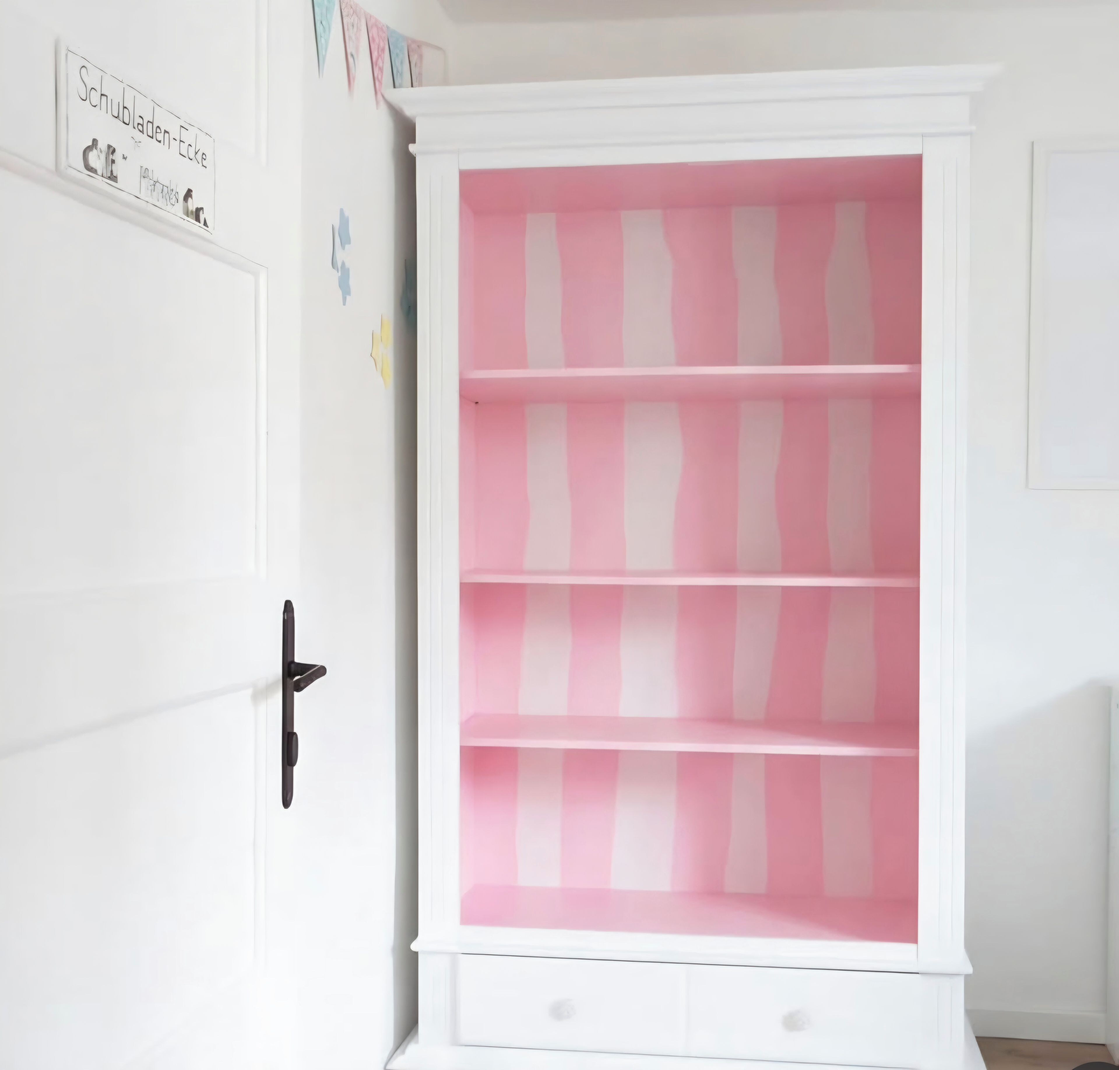 A white cabinet with pink and white striped shelves, a black handle, and a small drawer at the bottom.