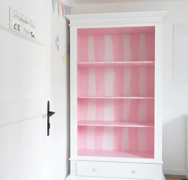 A white cabinet with pink and white striped shelves, a black handle, and a small drawer at the bottom.