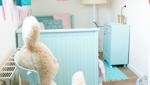 Habitació infantil amb un gran joguet de peluix, una cadira blava, una làmpada i una biblioteca plena de llibres per a nens.