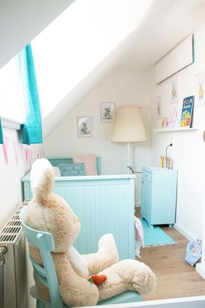 Ein Kinderzimmer mit einem großen Kuscheltier, einem blauen Stuhl, einer Lampe und einem Bücherregal mit Kinderbüchern.