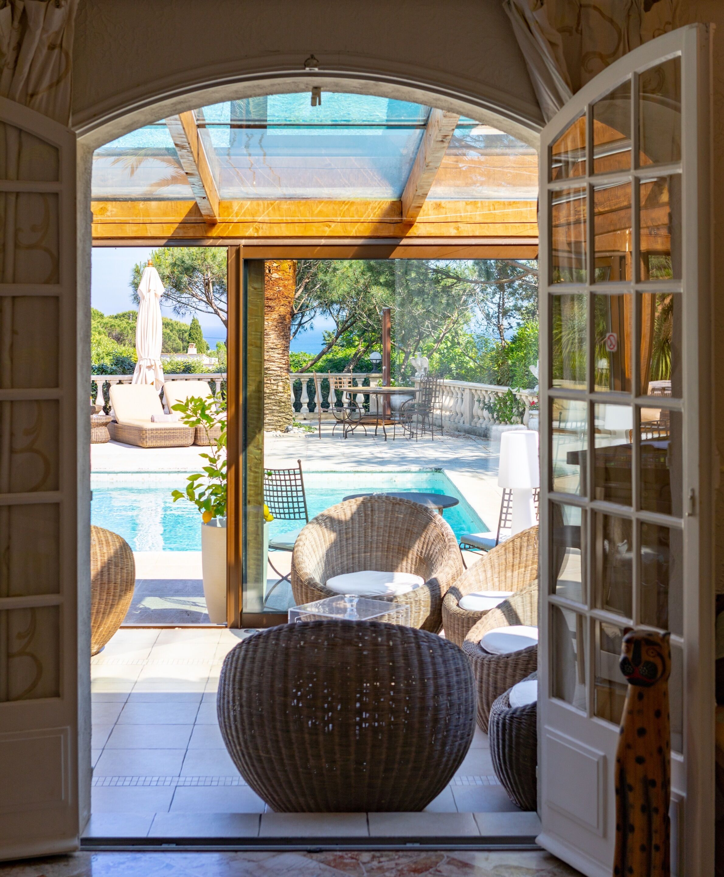 A view through a glass door into a pool area with wicker furniture and a fountain.