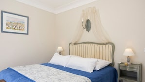 Een slaapkamer met een bed, twee nachtkastjes, een wandlamp en een lijst met een afbeelding.