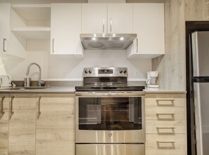 A modern kitchen with stainless steel appliances, wooden cabinets, and a built-in oven. - Stylish Studio Steps From Bell Centre (Montréal)