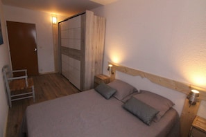 A bedroom with a bed, bedside lamps, a wooden headboard, a nightstand, and a chair. - 220m from ski slopes, 3rd floor, balcony, tv, ski locker, 60m², Alpe d'Huez (L'Alpe d'Huez)