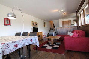 Ett vardagsrum med ett matbord, en röd soffa, en trappa och en tv.