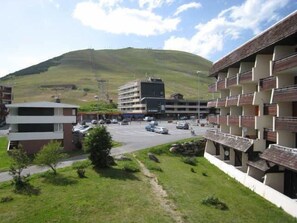 A hotel with a parking lot, a building with balconies, and a hill in the background. - 220m from ski slopes, 3rd floor, balcony, tv, ski locker, 60m², Alpe d'Huez (L'Alpe d'Huez)