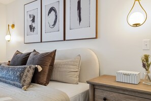 Ein Schlafzimmer mit einem Bett, Kissen, einem Nachttisch mit Lampe und Wandbildern.