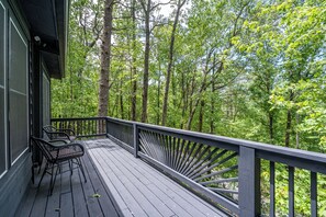 Um deck de madeira com duas cadeiras e guarda-corpo, com vista para uma floresta.