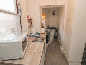 A narrow kitchen with a microwave, sink, and cabinets. - The Hyding Place (Whitby)