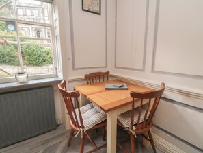 A corner dining area with a wooden table and chairs, a radiator, and a window with a view of buildings and greenery. - The Hyding Place (Whitby)
