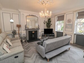 A living room with a fireplace, a television, a chandelier, and a sofa. - The Hyding Place (Whitby)