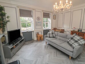 A living room with a grey sofa, a television, a chandelier, and a dining area with a table and chairs. - The Hyding Place (Whitby)