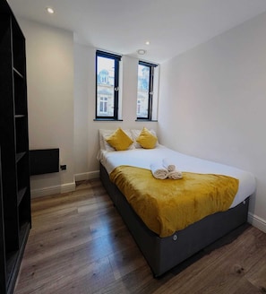 Ein modernes Schlafzimmer mit einem Bett, zwei Fenstern und Holzdielen.