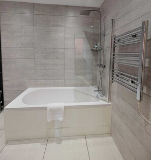 Un baño moderno con una bañera independiente, ducha con cerramiento de vidrio y toallero empotrado.