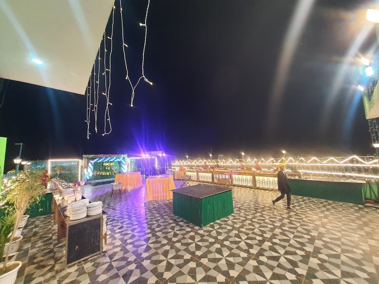 An outdoor event space with tables and chairs, a stage, and decorative lighting.