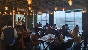 Restaurante com luminárias pendentes, mesas e cadeiras.