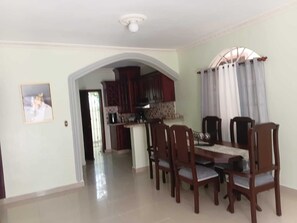 A dining area with a table and chairs, a kitchen in the background, and a door leading to another room. - Delightful 2-bedroom house with AC in Puerto Plata (Puerto Plata)