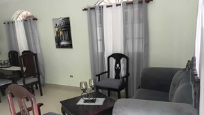 Ein Wohnzimmer mit Esstisch, zwei Stühlen, einer Couch und einer Zierlampe.