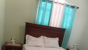 Ein Schlafzimmer mit einem hölzernen Bett, zwei Nachttischen, einem Fenster mit Vorhängen und einem kleinen Tisch mit einer Blume.