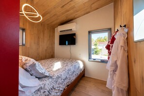 Quarto com cama, televisão, ar-condicionado, janela e roupão pendurado em um gancho.