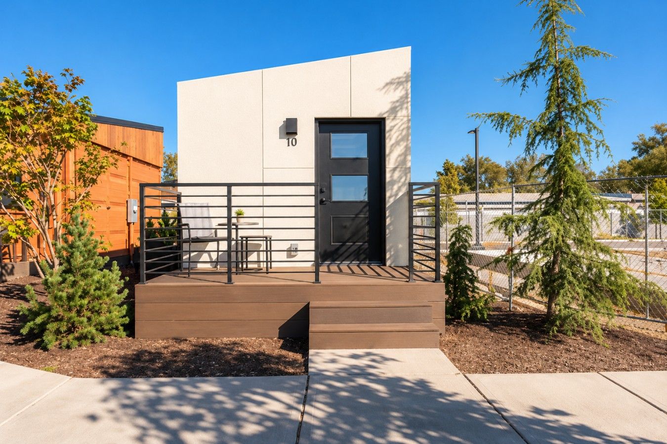 A modern building with a flat facade, a numbered door, and a small outdoor seating area with a table and chairs.