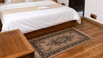 Quarto com cabeceira de madeira, uma cama grande com roupa de cama branca, uma pequena mesa de madeira e um tapete estampado.
