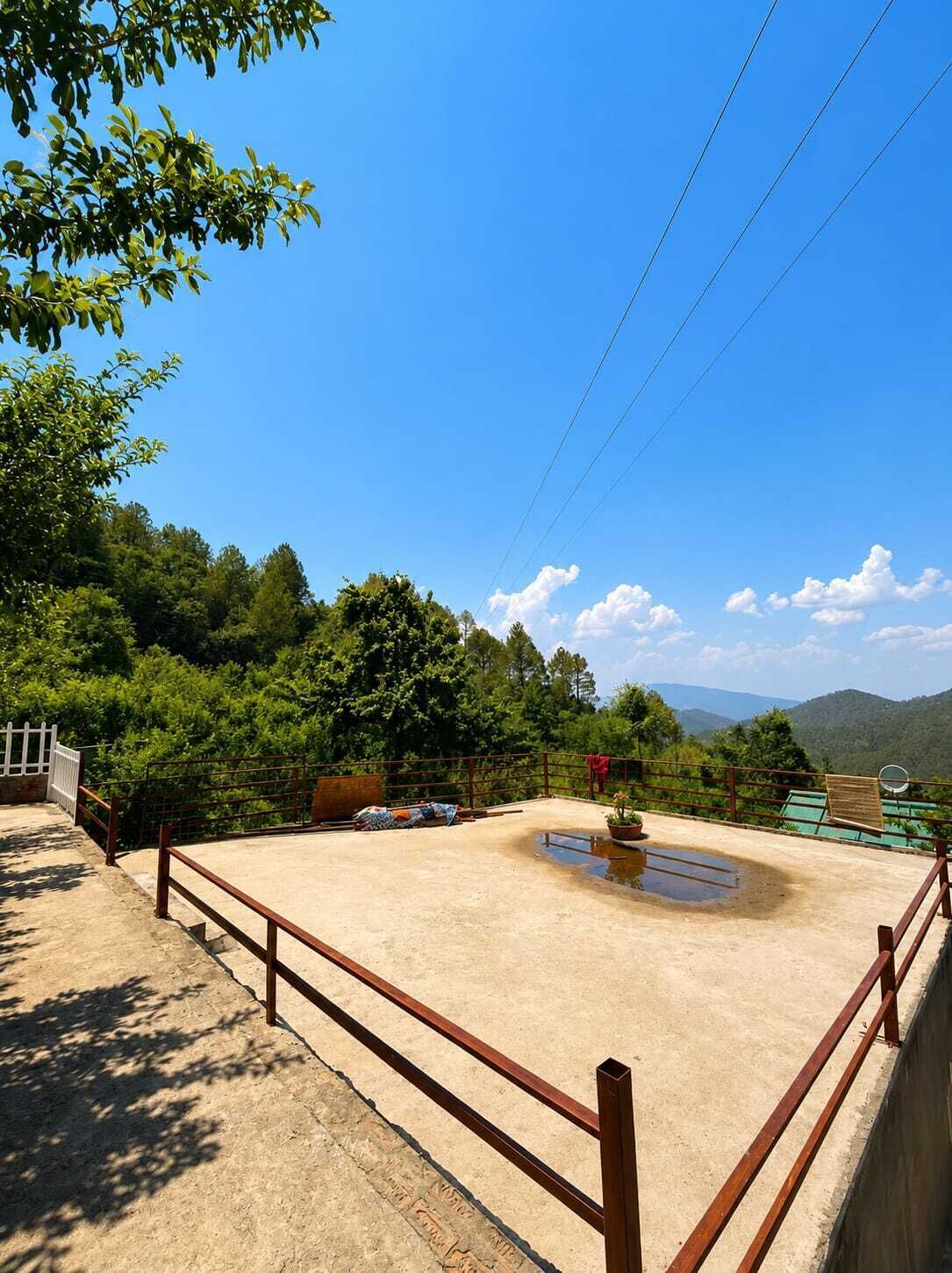 Un espacio exterior cercado con piso de concreto, rodeado de árboles y vistas a la montaña.