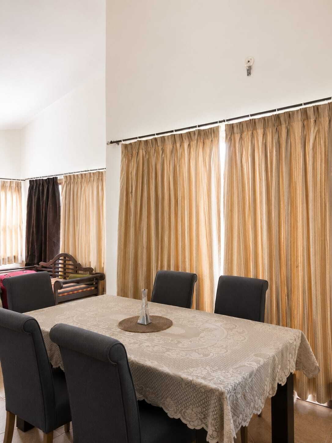 Comedor con una mesa preparada para cuatro personas, sillas, un jarrón decorativo y un fondo de cortina.