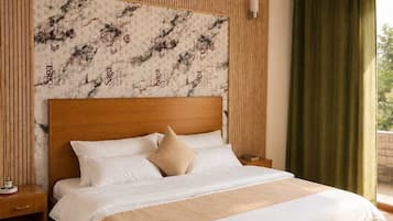Un dormitorio con cabecera de madera, una cama grande con ropa blanca, una mesita de noche y vistas a zonas verdes.