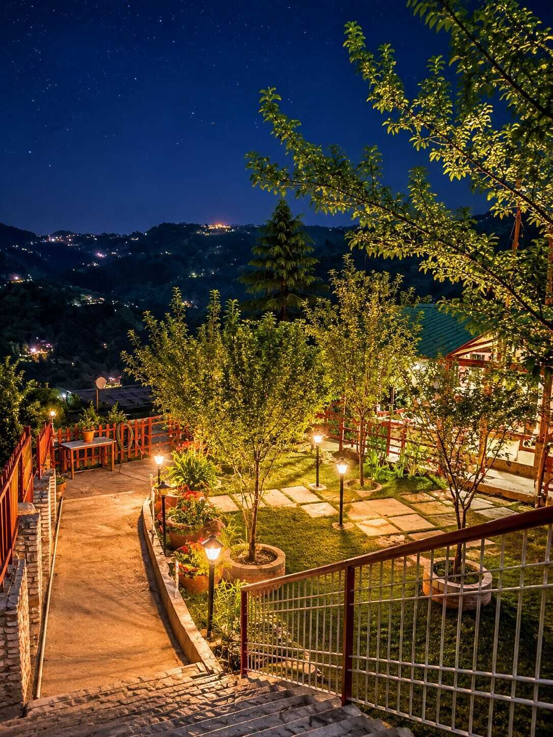 A nighttime outdoor area with a pathway leading to a building, surrounded by trees and illuminated by street lamps.