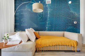 A modern living room with a sofa, a lamp, and a map-themed wall. - Modern 1BR APT w/ Balcony & Views -Beach Access (Hallandale Beach)
