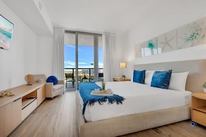 A modern hotel room with a large bed, a desk, a chair, and a balcony with a city view. - Modern 1BR APT w/ Balcony & Views -Beach Access (Hallandale Beach)